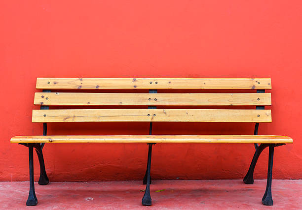 wooden long bench against blank red wall on background