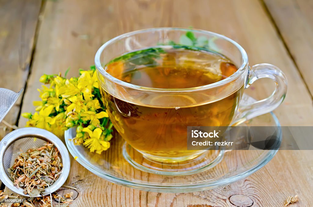 Herbal tea from tutsan in strainer with cup Tea in a glass cup, a metal filter for tea with dried flowers tutsan, Hypericum fresh flowers on the background of wooden boards Alternative Therapy Stock Photo