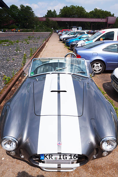 Essen, Germany - June 1, 2014: Bristish sportscar AC Shelby Cobra is standing on parking space on grounds of Zeche Zollverein. Convertible car.At right side are many more cars. In background people are walking.