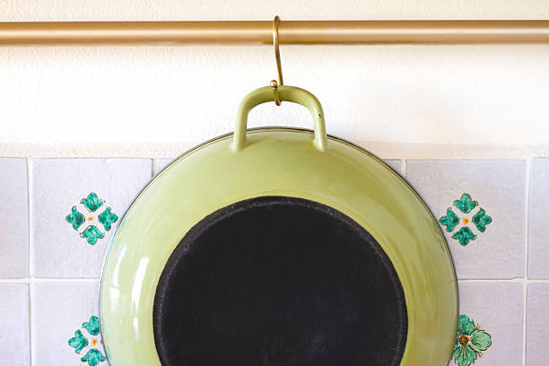 Green Enamel Frying Pan Hanging Against Pretty Floral Tile Backsplash