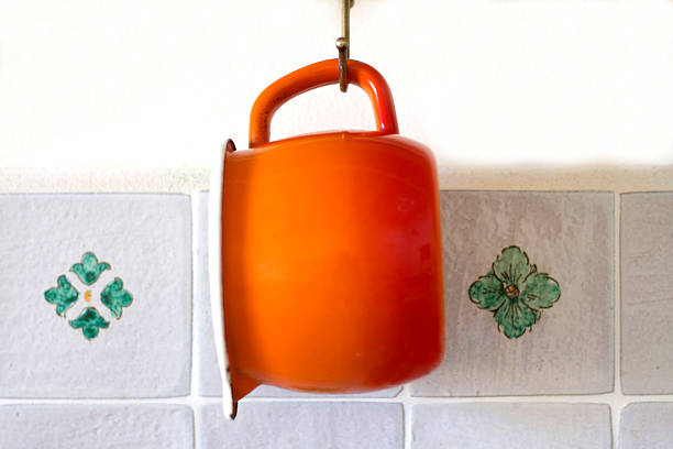 Bright Orange Enamel Pot Hanging Against Kitchen Floral Tile Backsplash