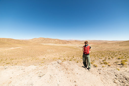 Barren mountain range and valley on the highlands of the Andes on the way to the famous Uyuni Salt Flat, among the most important travel destination in Bolivia. One person looking at camera in daylight.
