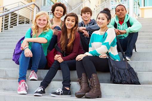 Portrait Of High School Students Sitting Outside Building Smiling To Camera