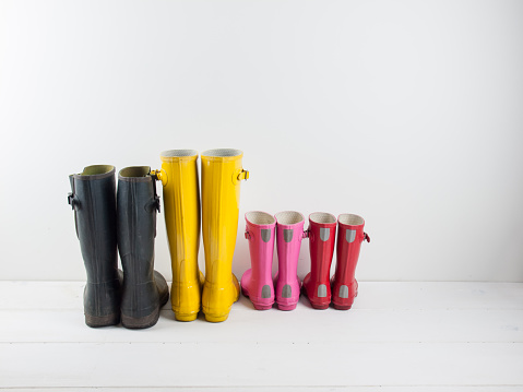 four pairs of colourful rubber rain boots  on a white rustic floor infront of a white wall