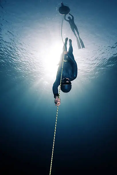 Lady free diver descending along the rope linked to the buoy on surface. Free immersion discipline