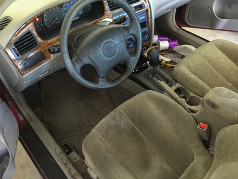 Run Down Car Interior, car cabin cluttered with fast food cups and trash showing run down fabric and faux leather trip of stirring wheel and dirty dashboard console