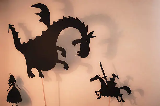 Black silhouettes of Dragon, Princess and Knight with bright glowing screen of shadow theatre in the background.
