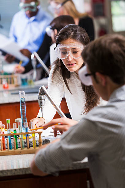 University or high school students in chemistry class Multi-ethnic group of students in chemistry lab.  Focus on Hispanic girl (18 years) in foreground, wearing safety goggles, doing an experiment with chemicals in test tubes. high school high school student science multi ethnic group stock pictures, royalty-free photos & images