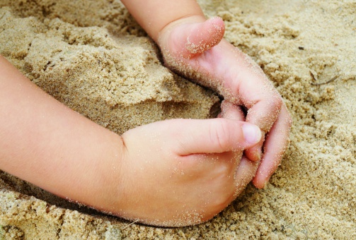 Small child hands playing in the sand at the beach.