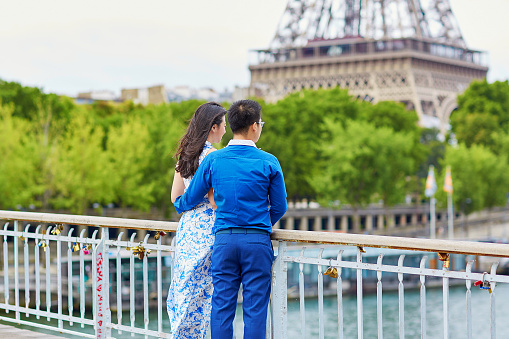 Young romantic Asian couple having a date on the bridge over the Seine near the Eiffel Tower, Paris, France