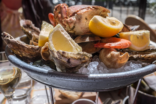 A seafood platter has been served at a Parisian outdoor sidewalk restaurant on a sunny day in spring (or early summer). The food has been placed on crushed ice to keep it chilled. The platter contains oysters, crab, shrimps and pieces of lemon.