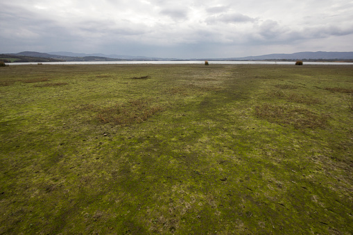 Flat grassy lake shore after the withdrawal of water. Photo is taken with dslr camera and wide angle lens on cloudy autumn day in European countryside.
