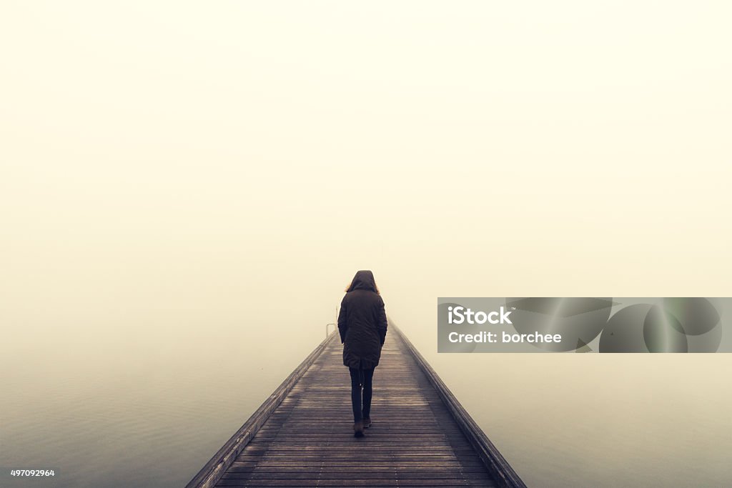 Woman Crossing The Bridge Woman crossing the bridge over lake on a foggy winter day. Fog Stock Photo