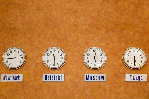 World time clocks, orange wall, horizontal orientation.