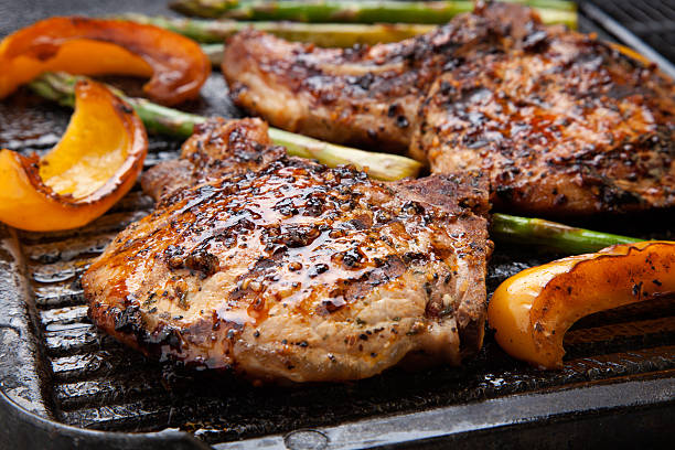 Grilling Pork Chops Juicy pork chops are grilled on griddle with asparagus and bell pepper. Backyard grilling for summer picnic. barbecue pork stock pictures, royalty-free photos & images
