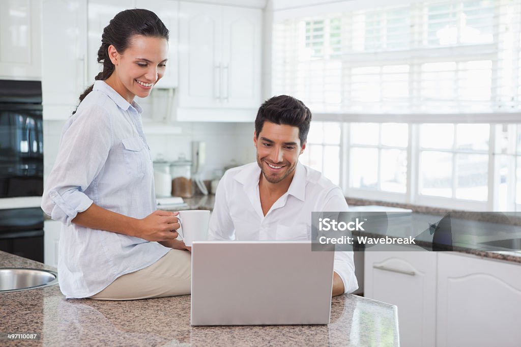 Happy couple using laptop together at the counter Happy couple using laptop together at the counter at home in kitchen 20-29 Years Stock Photo