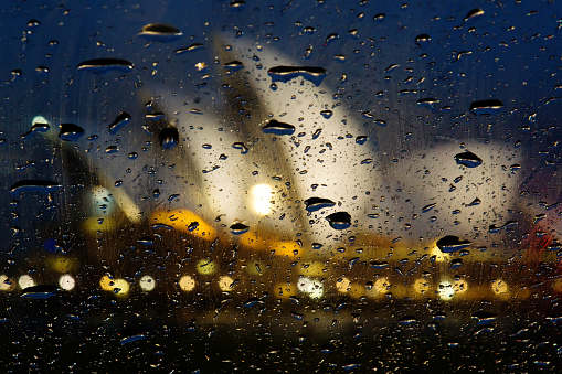 Close-up of illuminated traffic lights and raindrops seen through transparent glass window.