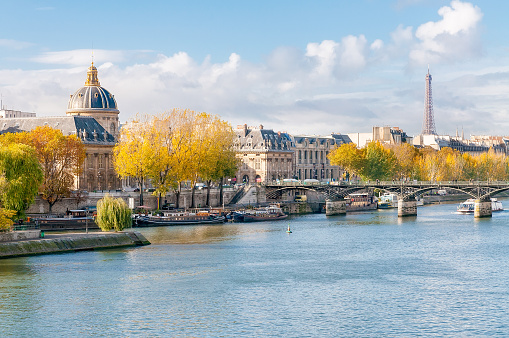The Seine, the French Academy, the Pont des Arts and the Eiffel tower seen from the Pont Neuf in Paris. Houseboats moored at the dock.