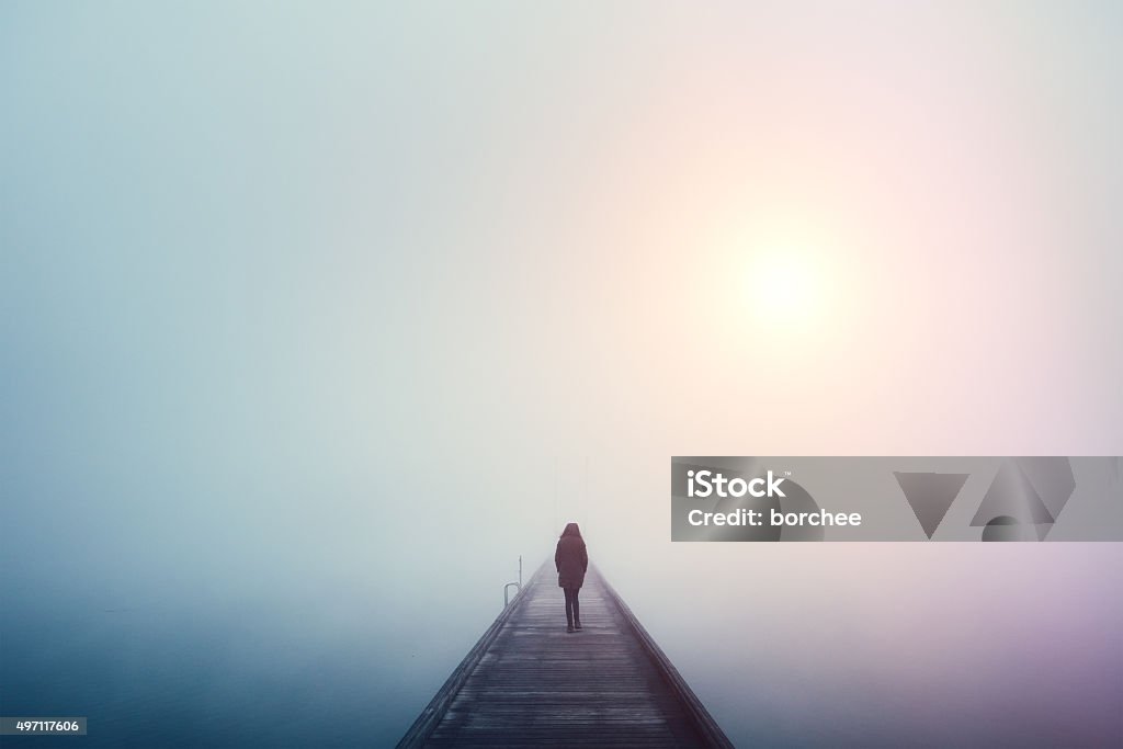 Crossing The Bridge Woman crossing the bridge over lake on a foggy winter day. Loneliness Stock Photo