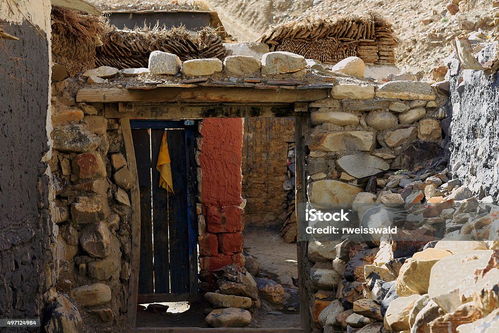 Wooden door in stone wall. Sakya-Tibet. 1826 Wooden door open-not very solid stone wall -second wall topped with cow+yak dungs-ruins of ancient North Seat of Sakya-Grey Soil monastery on Ponpori Hill-right bank of Chong Chu-river. Sakya-Tibet. 2015 Stock Photo
