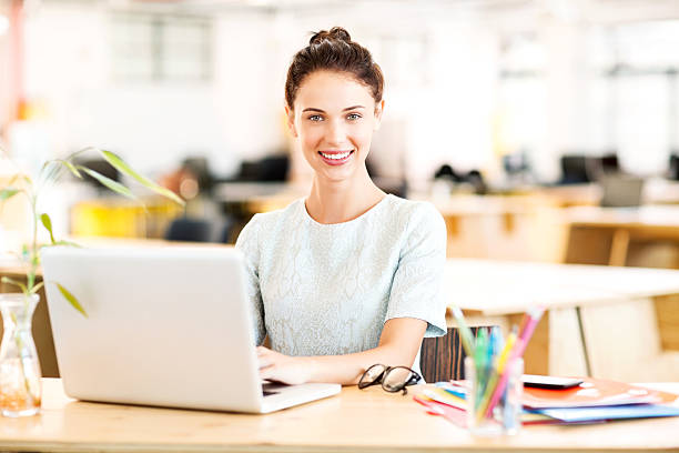 Portrait of confident businesswoman using laptop at desk in office. Horizontal shot.