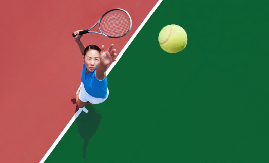 Young Asian woman serving tennis ball.