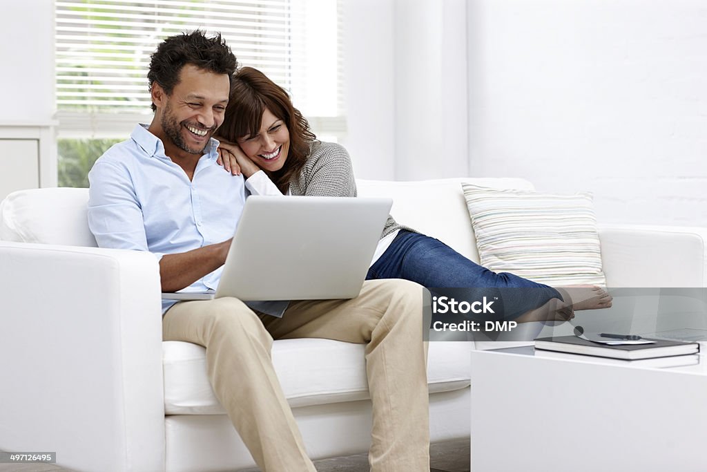 Cheerful couple using laptop at home Cheerful couple relaxing together on couch surfing internet on laptop at home Couple - Relationship Stock Photo