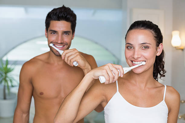 привлекательные пара улыбка во время использования электрический toothbrushes - электрическая зубная щётка стоковые фото и изображения