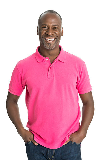 Mature African Man Smiling Portrait of happy mature man in casuals standing with hands in pockets against white background polo shirt stock pictures, royalty-free photos & images