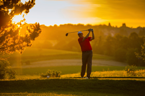 Mid adult golfer teeing of at sunset.