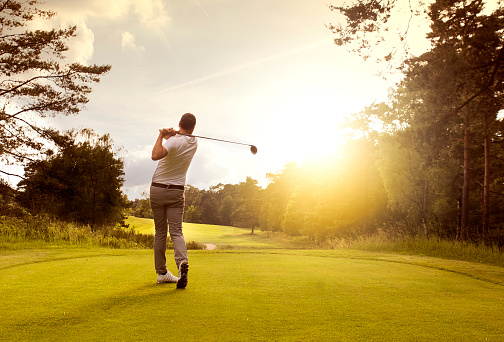 A golfer is celebrating a hole at sunset on the green. Silhouette style image with copy space.