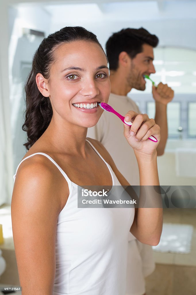 Women smiles with toothbrush in hand while boyfriend brushes tee Women smiles with toothbrush in hand while boyfriend brushes teeth at home in bathroom 20-29 Years Stock Photo