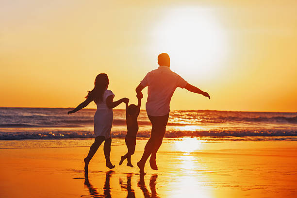 Happy family with child have a fun on sunset beach Happy family - father, mother, baby son hold hands and run with fun along edge of sunset sea on black sand beach. Active parents and people outdoor activity on tropical summer vacations with children. raro stock pictures, royalty-free photos & images