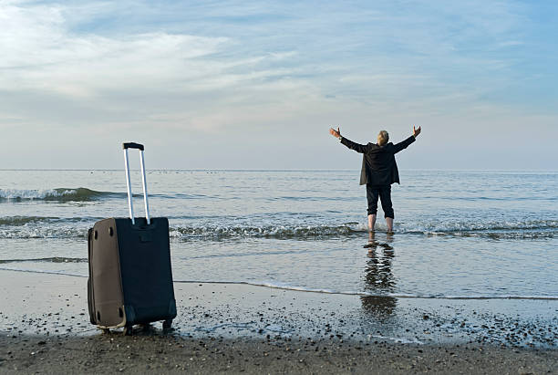 istock Businessman standing barefooted at beach in water raising arms 497142738