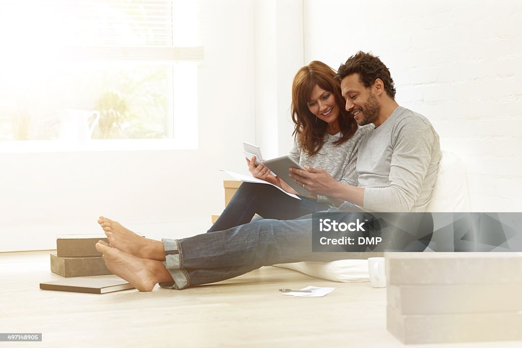 Happy couple sitting together calculating their expenses Portrait of happy couple sitting together calculating their expenses with help of calculator and digital tablet Couple - Relationship Stock Photo