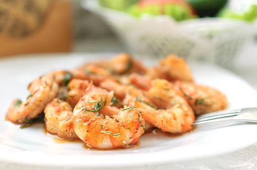 Fried black tiger prawns with herbs and spices on a white plate.