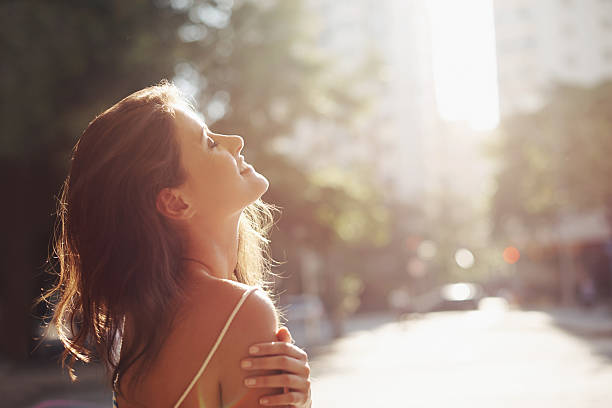 Enjoying the sun on her skin Cropped shot of a beautiful young woman standing in a city touch of the sun stock pictures, royalty-free photos & images