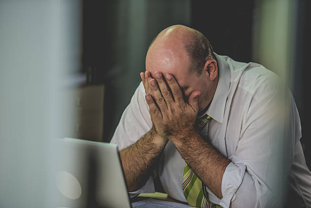 Frustrated office worker with his head in his hands Distressed white collar worker sitting in front of a computer with his head in his hands. computer bug photos stock pictures, royalty-free photos & images