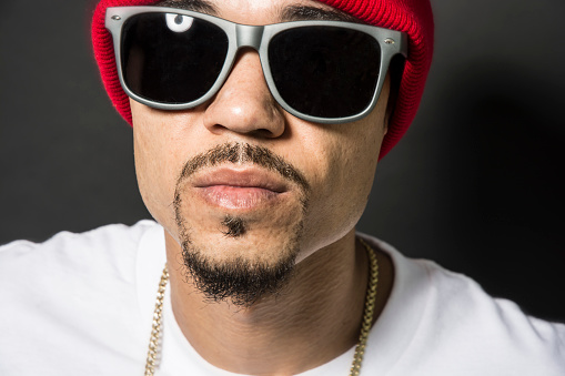 Male Rapper Hip Hop Artist In Sunglasses And Red Cap against gray black background