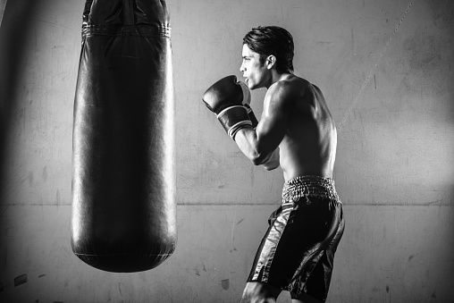 Hispanic Man Hitting a Punching Bag in Black and White.  Against a grungy concrete wall.Hispanic Man Hitting a Punching Bag in Black and White.  Against a grungy concrete wall.