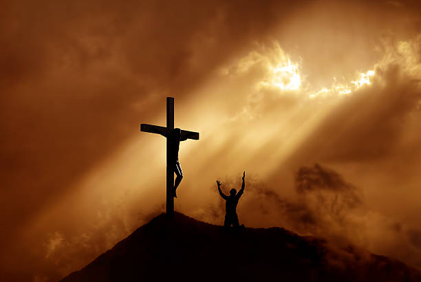 Dramatic sky scenery with mountain cross and a worshiper Silhouette of a man praying before a cross at sunset concept of religion crucifix photos stock pictures, royalty-free photos & images