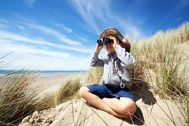 Child explorer at the beach Little boy searching with binoculars at the beach dressed as explorer concept for nature, discovery, exploring and education bird watching stock pictures, royalty-free photos & images