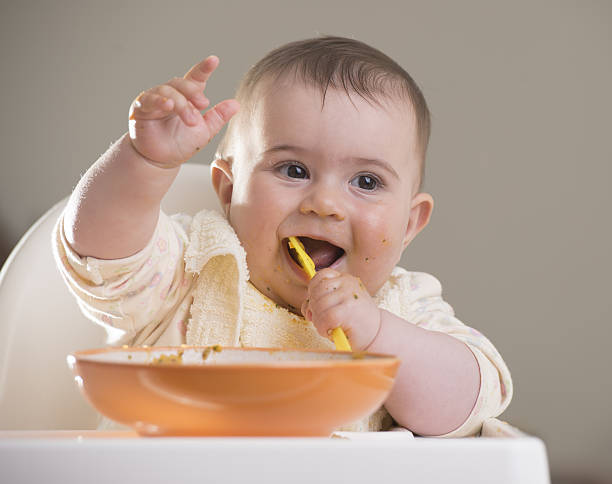 istock baby girl eating with yellow spoon 497185085