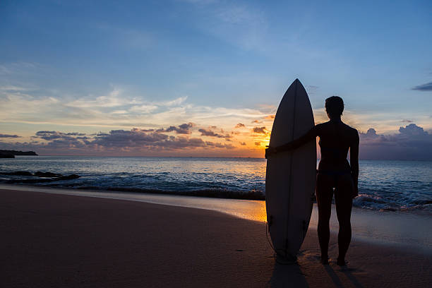 istock woman surfer with surfboard on tropical beach at sunset 497186079