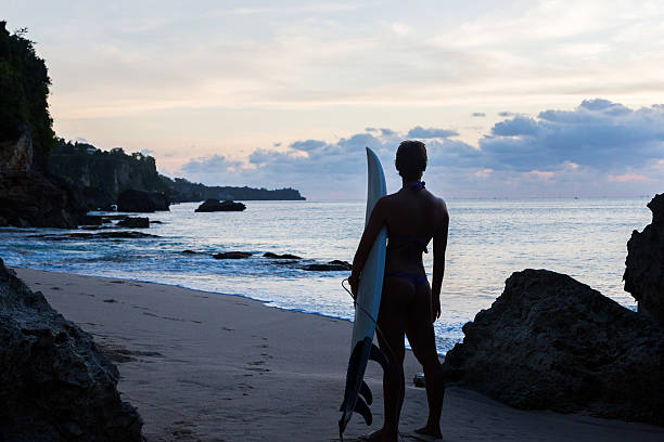 istock woman surfer with surfboard on tropical beach at sunset 497186093