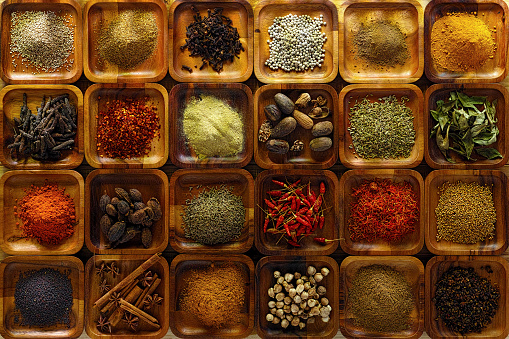 A large selection of commonly used Indian cooking spices in wooden trays on an old table. Spices include, chili ,cumin, tumeric, corriander, cumin, cardamon, garam masala, saffron, cinamon and star anise, poppy seed, sesame, cloves, nutmeg, black and white pepper corns, aniseed and fenugreek.