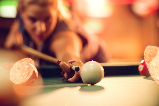 Close up of a woman playing billiard and aiming at white ball.