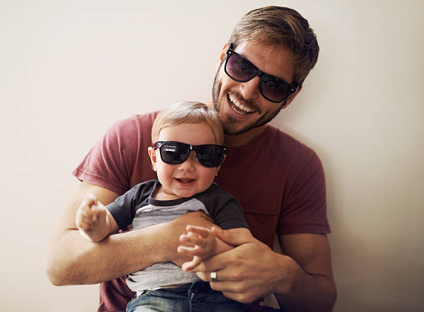 Coolness runs in this family! A young father and his infant son wearing matching sunglasses and laughing fashionable dad stock pictures, royalty-free photos & images