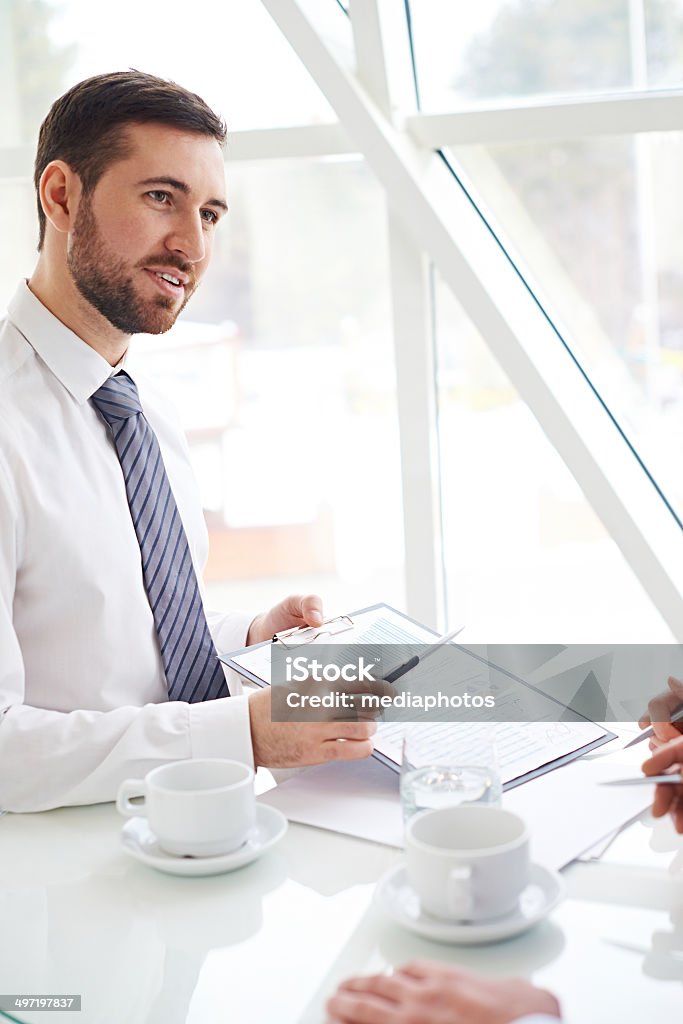 Discussing a document Bearded businessman showing document in clipboard to business partners at meeting Financial Report Stock Photo