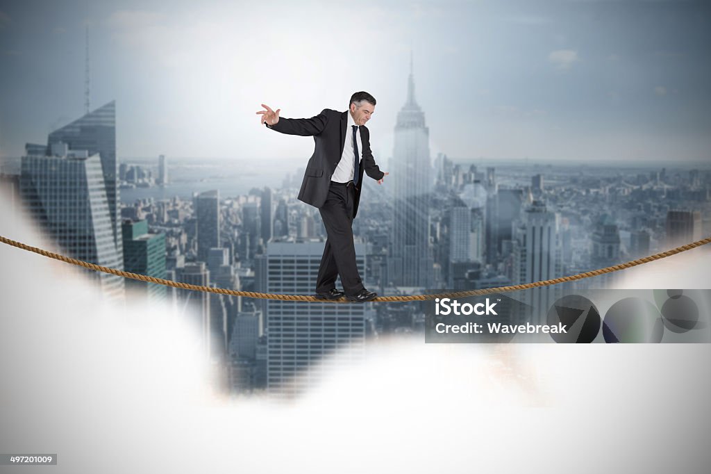 Composite image of mature businessman doing a balancing act Composite image of mature businessman doing a balancing act against cityscape 50-59 Years Stock Photo